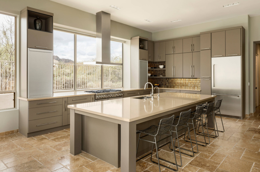 Inredning av ett modernt kök, med en undermonterad diskho, släta luckor, bänkskiva i kvarts, stänkskydd i glaskakel, rostfria vitvaror, travertin golv, en köksö och brunt golv