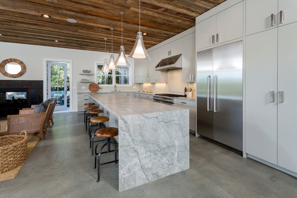 Inspiration for a contemporary galley kitchen in San Francisco with a submerged sink, flat-panel cabinets, white cabinets, white splashback, metro tiled splashback, stainless steel appliances, concrete flooring, an island, grey floors and grey worktops.