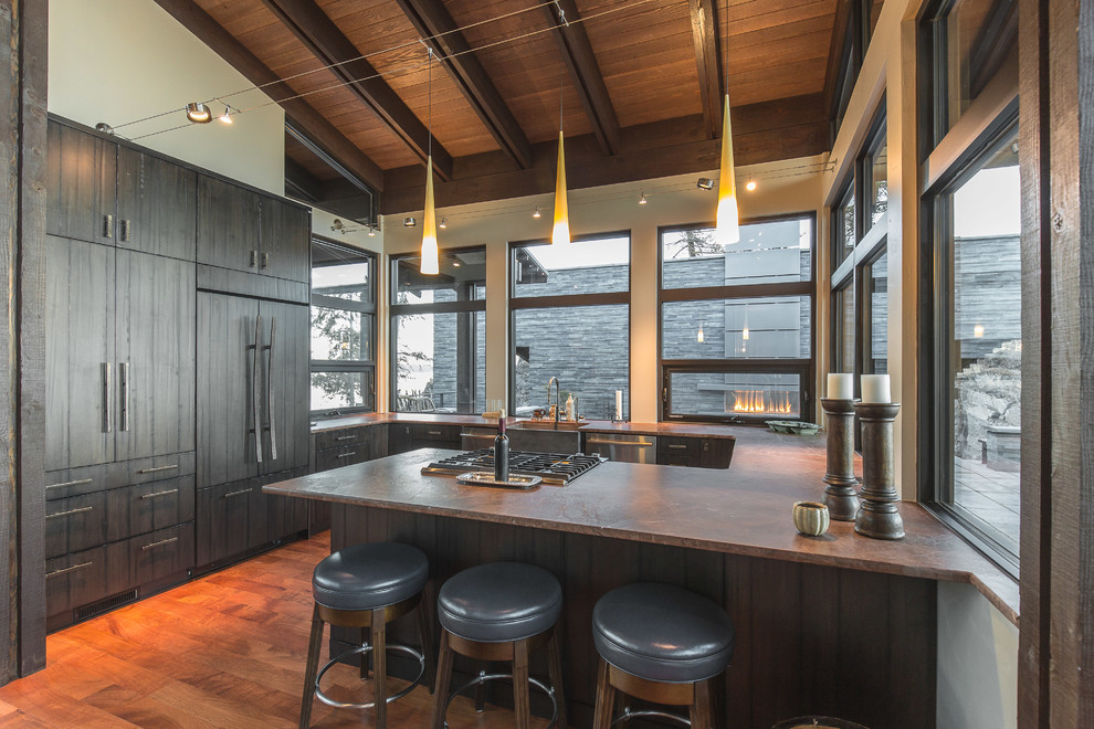 This is an example of a rustic u-shaped kitchen in Other with a belfast sink, flat-panel cabinets, dark wood cabinets, window splashback, stainless steel appliances, medium hardwood flooring, a breakfast bar, brown floors and brown worktops.