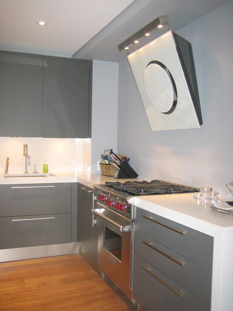 Example of a mid-sized minimalist l-shaped light wood floor and brown floor eat-in kitchen design in New York with an undermount sink, flat-panel cabinets, gray cabinets, solid surface countertops, white backsplash, stainless steel appliances and an island