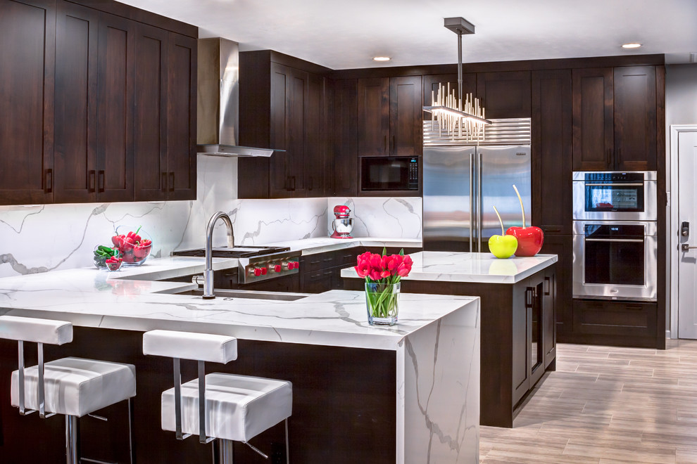 Eat-in kitchen - large contemporary u-shaped light wood floor eat-in kitchen idea in Houston with a farmhouse sink, shaker cabinets, dark wood cabinets, white backsplash, porcelain backsplash, stainless steel appliances and an island