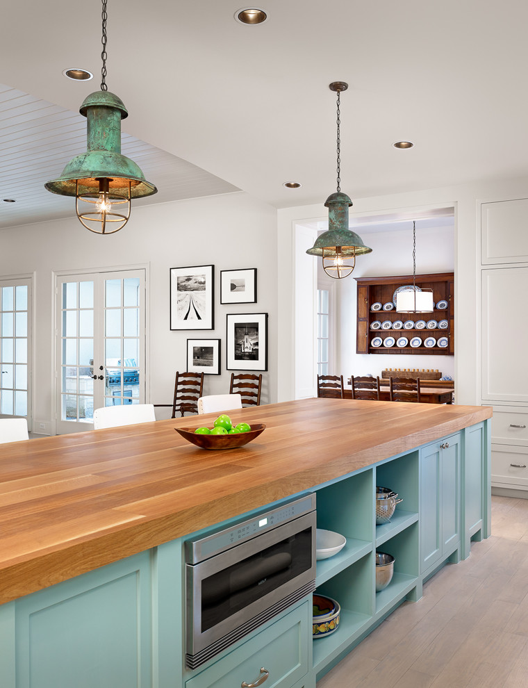 Klassisk inredning av ett stort kök, med luckor med infälld panel, blå skåp, träbänkskiva, rostfria vitvaror, ljust trägolv och en köksö