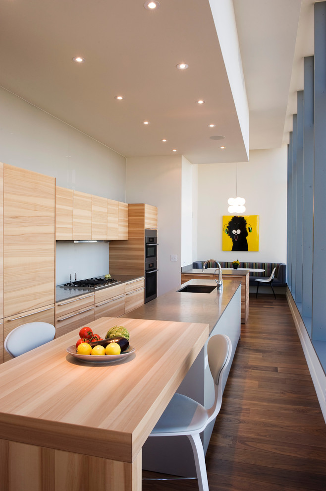 На фото: параллельная кухня в современном стиле с обеденным столом, плоскими фасадами, светлыми деревянными фасадами, темным паркетным полом, островом и окном с