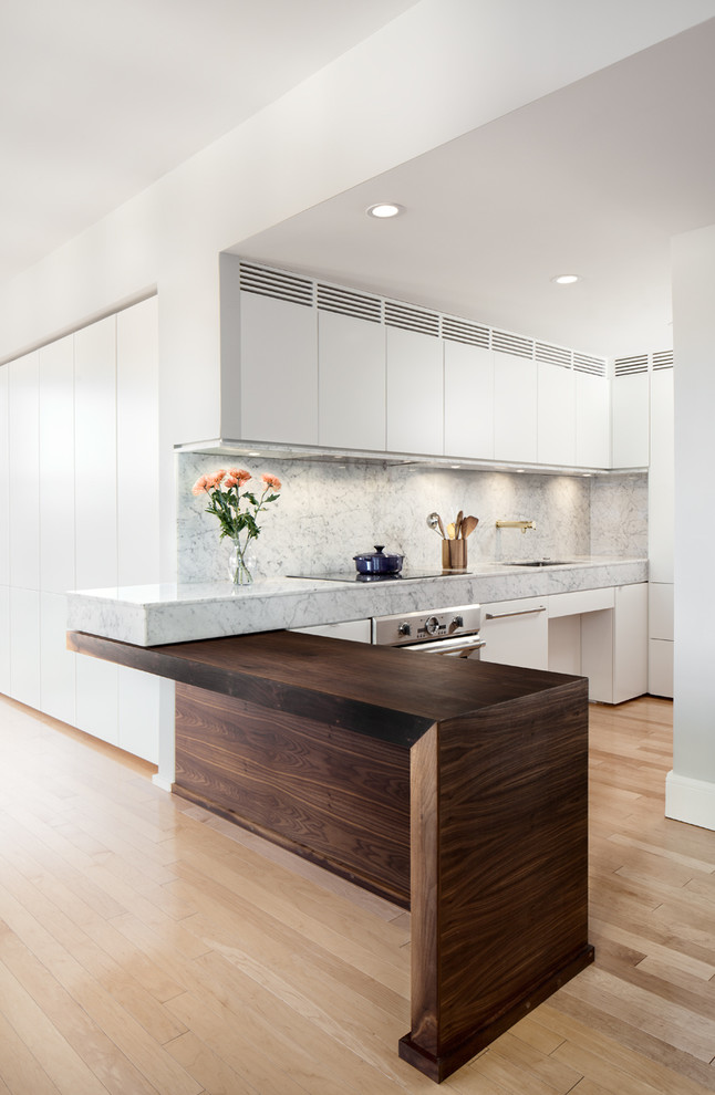 Inspiration for a medium sized modern l-shaped kitchen/diner in Boston with a submerged sink, flat-panel cabinets, white cabinets, marble worktops, integrated appliances, light hardwood flooring and a breakfast bar.
