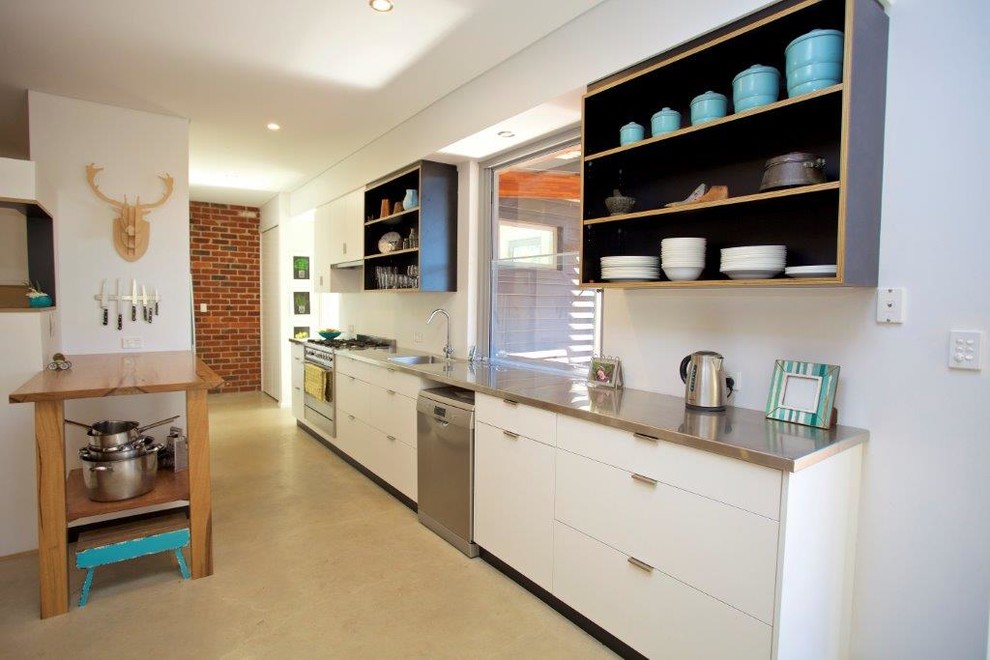 Foto di una cucina lineare minimal con lavello integrato, ante bianche, top in acciaio inossidabile, elettrodomestici in acciaio inossidabile e pavimento in cemento