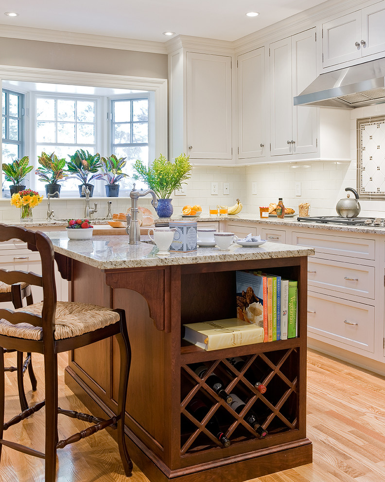 Inspiration for a mid-sized timeless l-shaped light wood floor and brown floor kitchen remodel in Boston with an undermount sink, recessed-panel cabinets, white cabinets, granite countertops, white backsplash, subway tile backsplash, paneled appliances, an island and multicolored countertops
