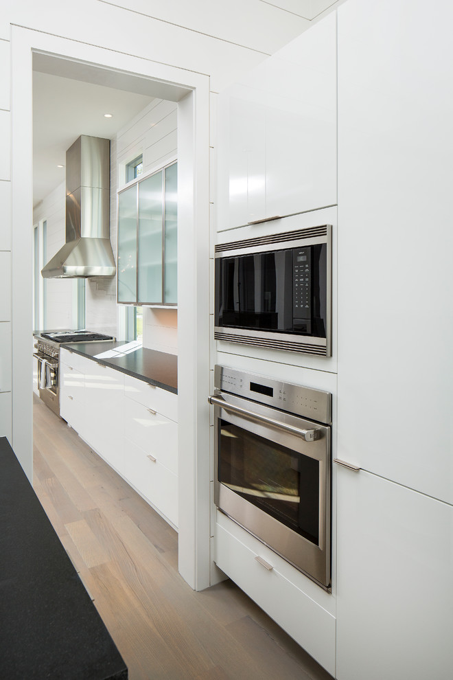 Large contemporary l-shaped kitchen/diner in Charleston with a submerged sink, flat-panel cabinets, white cabinets, granite worktops, white splashback, marble splashback, stainless steel appliances, medium hardwood flooring, an island and grey floors.