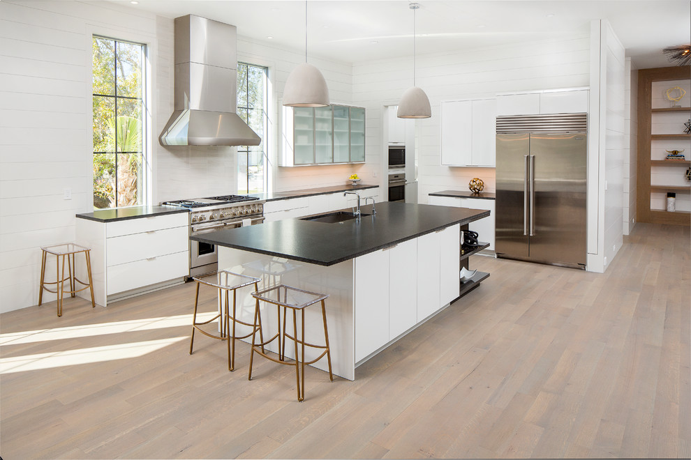 Inspiration for a large contemporary l-shaped kitchen/diner in Charleston with a submerged sink, flat-panel cabinets, white cabinets, granite worktops, white splashback, marble splashback, stainless steel appliances, medium hardwood flooring, an island and grey floors.