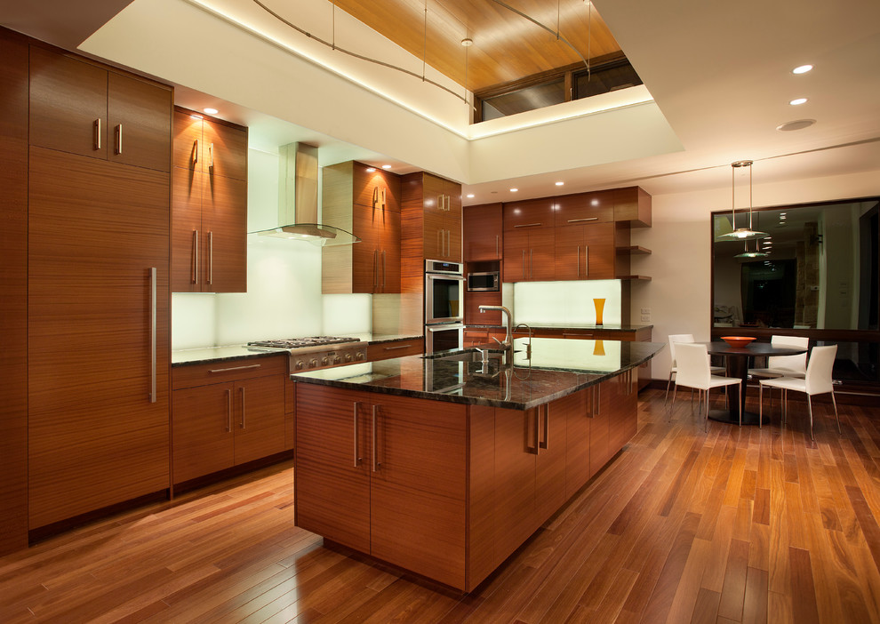 Cette image montre une grande cuisine américaine minimaliste en L et bois brun avec un placard à porte plane, un électroménager en acier inoxydable, un sol en bois brun et îlot.