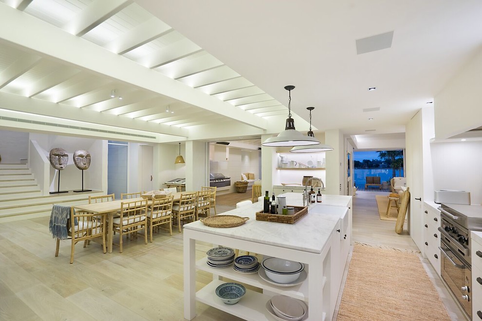 Expansive beach style single-wall open plan kitchen in Central Coast with an island, shaker cabinets, white cabinets, marble worktops, white splashback, metro tiled splashback, stainless steel appliances and a belfast sink.