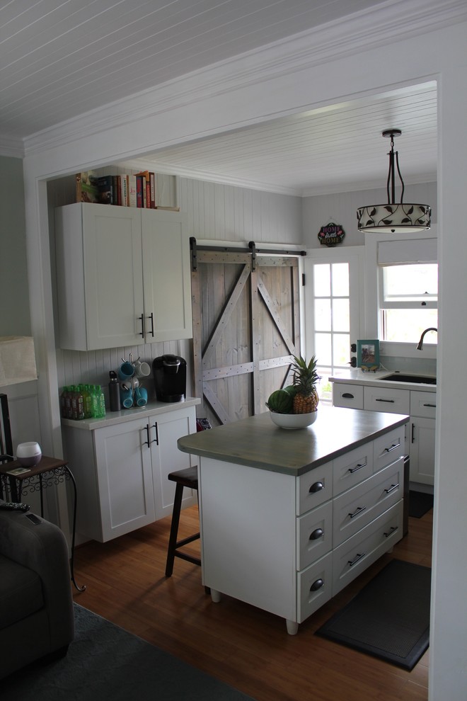 Maritim inredning av ett litet kök, med en undermonterad diskho, släta luckor, vita skåp, bänkskiva i kvartsit, blått stänkskydd, stänkskydd i glaskakel, rostfria vitvaror, bambugolv, en köksö och brunt golv