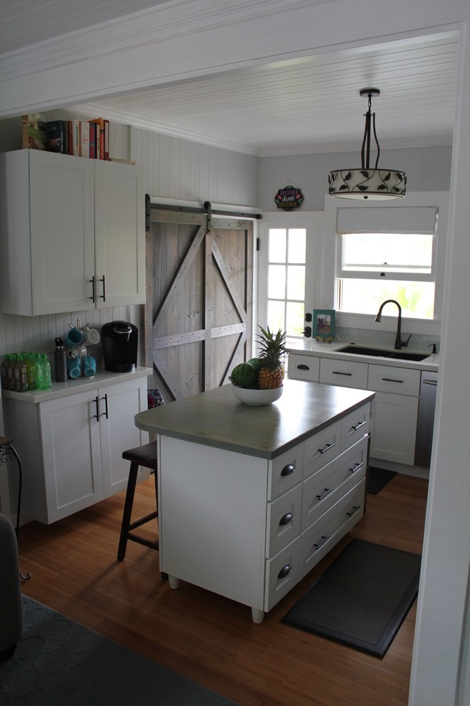 Bild på ett litet maritimt kök, med en undermonterad diskho, släta luckor, vita skåp, bänkskiva i kvartsit, blått stänkskydd, stänkskydd i glaskakel, rostfria vitvaror, bambugolv, en köksö och brunt golv