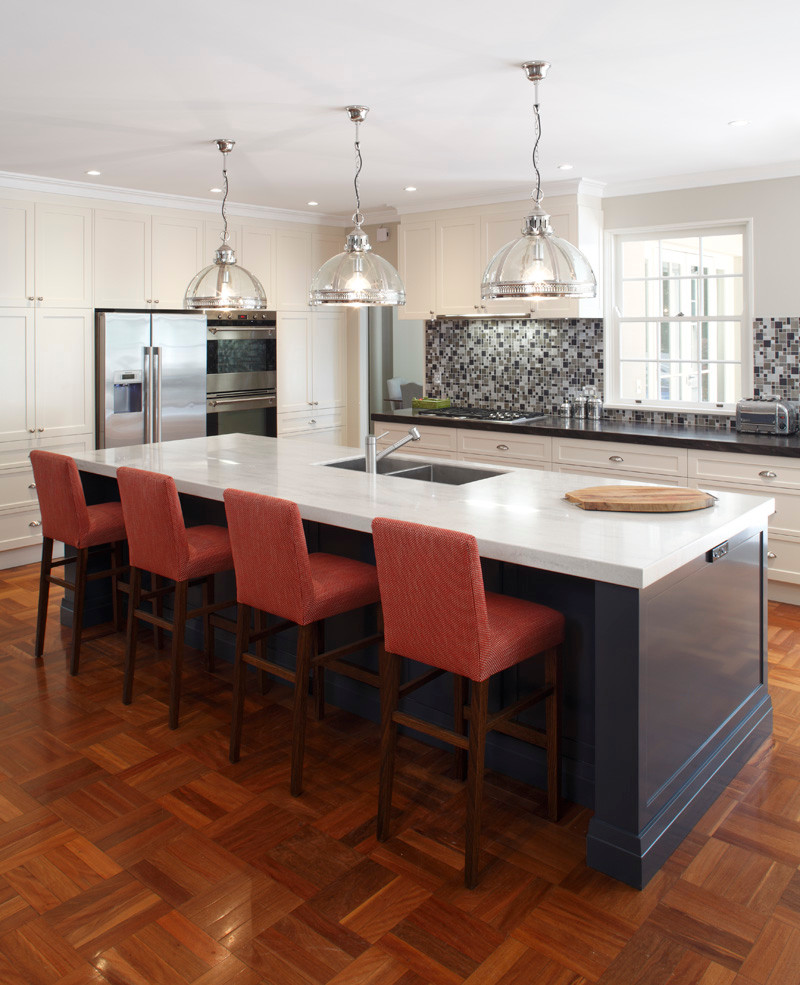 Medium sized traditional l-shaped open plan kitchen in Sydney with a double-bowl sink, shaker cabinets, white cabinets, composite countertops, metallic splashback, glass tiled splashback, stainless steel appliances, medium hardwood flooring and an island.