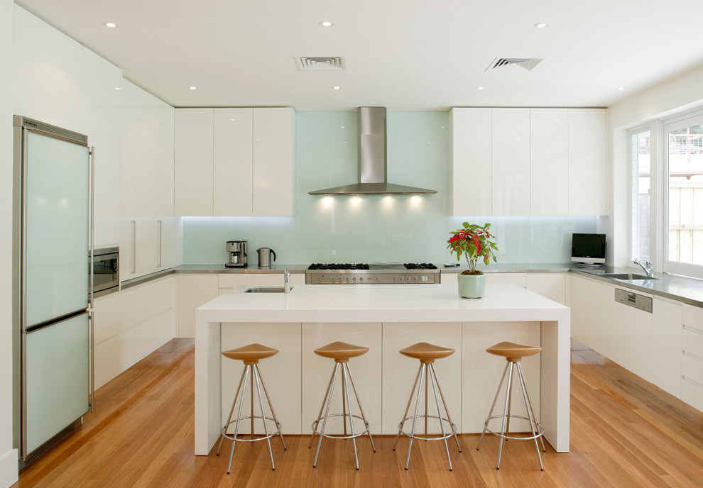 シドニーにある高級な広いコンテンポラリースタイルのおしゃれなキッチン (アンダーカウンターシンク、フラットパネル扉のキャビネット、白いキャビネット、ステンレスカウンター、緑のキッチンパネル、ガラス板のキッチンパネル、シルバーの調理設備、無垢フローリング) の写真