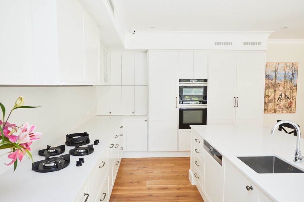 シドニーにあるコンテンポラリースタイルのおしゃれなキッチン (シングルシンク、白いキャビネット、白いキッチンパネル、パネルと同色の調理設備、無垢フローリング、白いキッチンカウンター、大理石カウンター) の写真