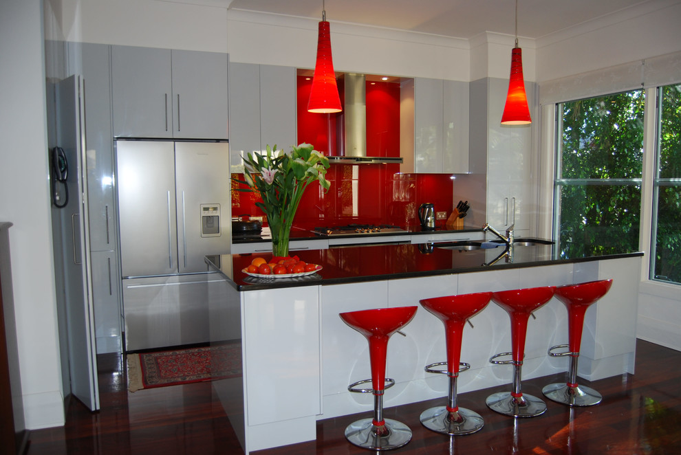 Mittelgroße Moderne Wohnküche in L-Form mit flächenbündigen Schrankfronten, weißen Schränken, Küchenrückwand in Rot, Glasrückwand, Küchengeräten aus Edelstahl, Unterbauwaschbecken, dunklem Holzboden und Kücheninsel in Sydney