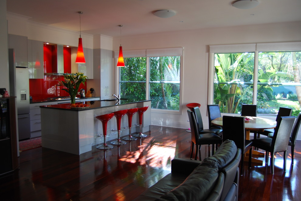 シドニーにあるラグジュアリーな中くらいなコンテンポラリースタイルのおしゃれなキッチン (アンダーカウンターシンク、フラットパネル扉のキャビネット、白いキャビネット、赤いキッチンパネル、ガラス板のキッチンパネル、シルバーの調理設備、濃色無垢フローリング) の写真