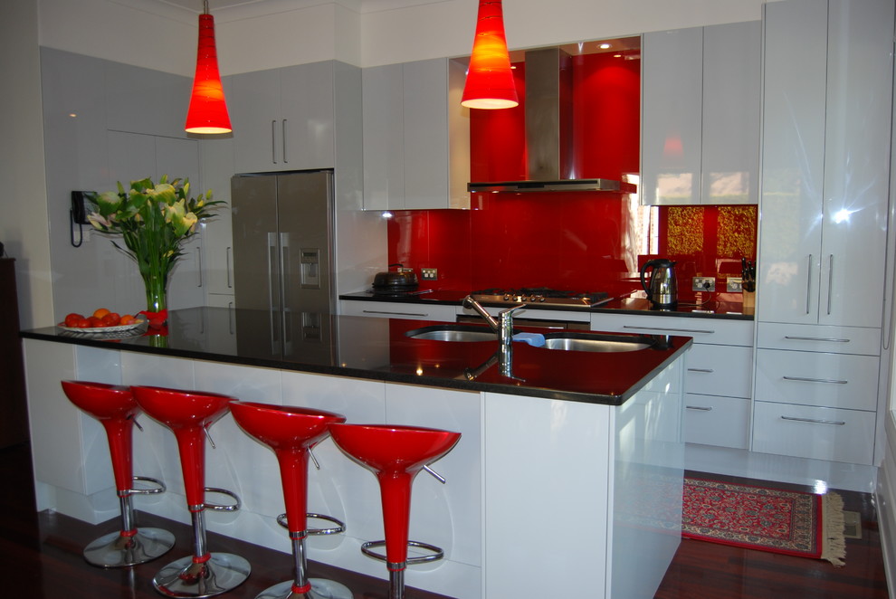 Mid-sized trendy l-shaped dark wood floor eat-in kitchen photo in Sydney with an undermount sink, flat-panel cabinets, white cabinets, red backsplash, glass sheet backsplash, stainless steel appliances and an island