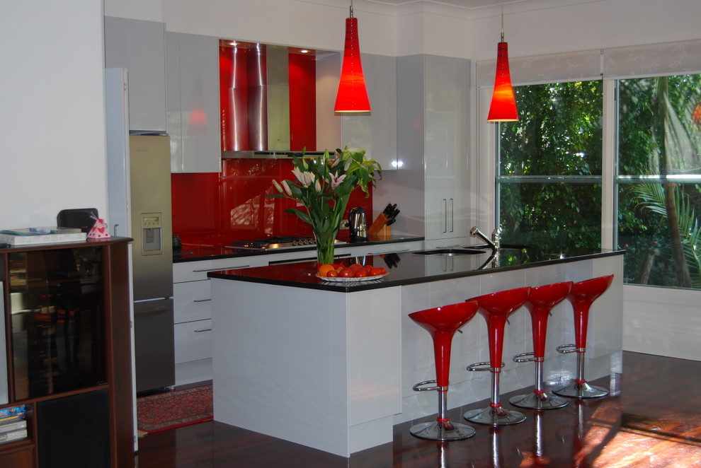 Immagine di una cucina minimal di medie dimensioni con lavello sottopiano, ante lisce, ante bianche, paraspruzzi rosso, paraspruzzi con lastra di vetro, elettrodomestici in acciaio inossidabile e parquet scuro