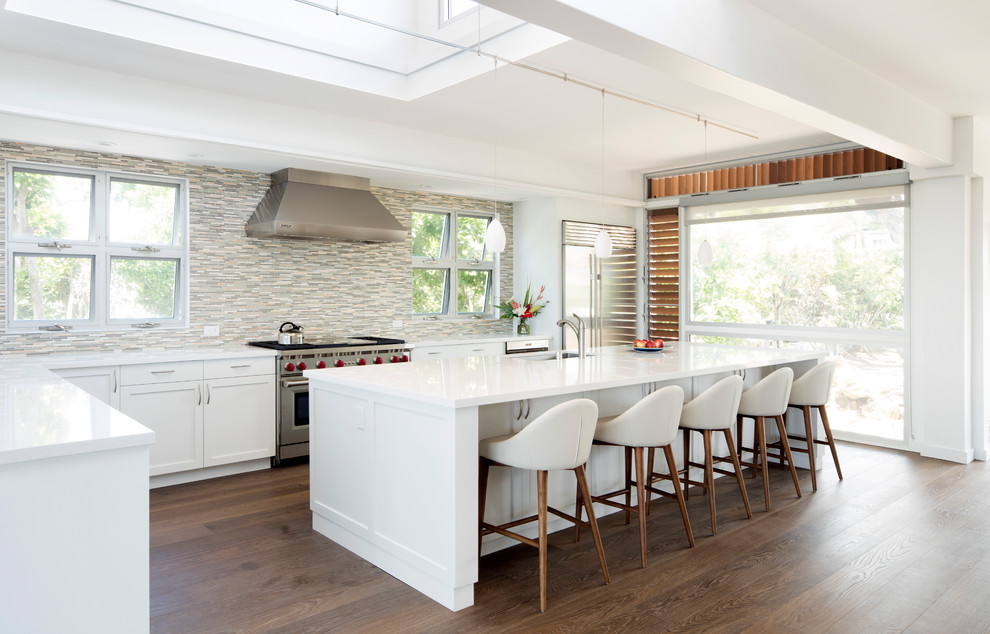 Inspiration for a large world-inspired l-shaped open plan kitchen in Hawaii with a submerged sink, shaker cabinets, white cabinets, multi-coloured splashback, matchstick tiled splashback, stainless steel appliances, dark hardwood flooring, an island, brown floors, white worktops and composite countertops.