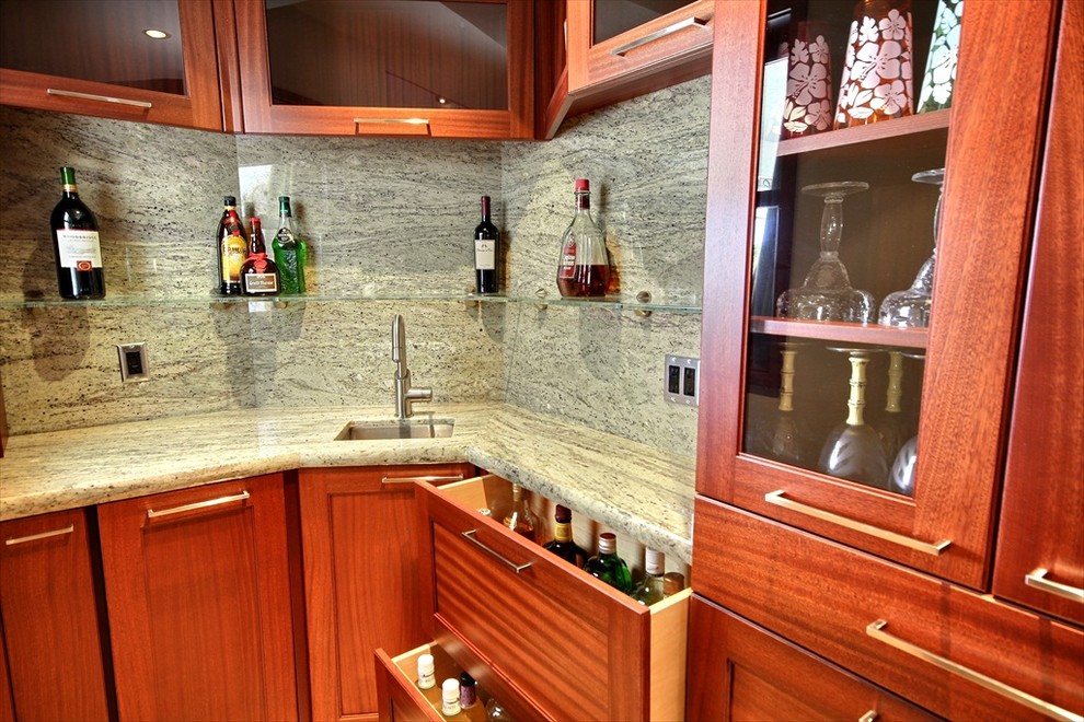 Exotisk inredning av ett litet l-kök, med en enkel diskho, luckor med infälld panel, skåp i mellenmörkt trä, granitbänkskiva, travertin golv och en halv köksö