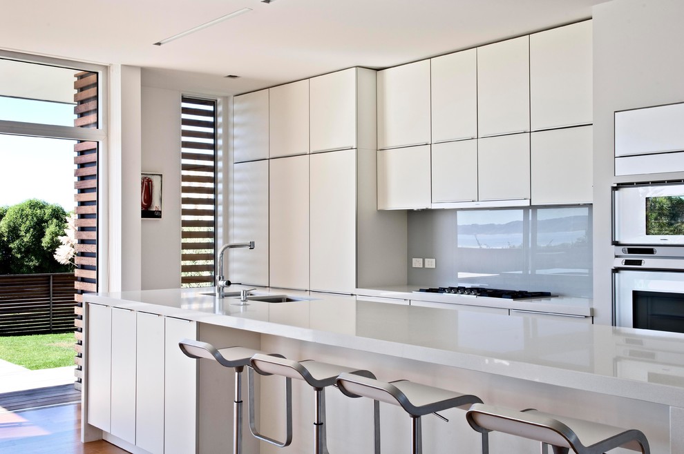 Idéer för ett modernt kök och matrum, med en dubbel diskho, vita skåp, bänkskiva i kvarts, grått stänkskydd, glaspanel som stänkskydd, rostfria vitvaror, ljust trägolv och en köksö