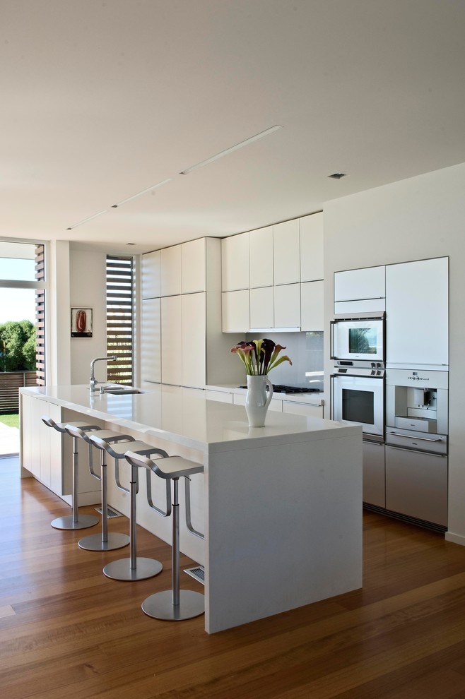 Inspiration for a contemporary light wood floor eat-in kitchen remodel in Wellington with a double-bowl sink, white cabinets, quartz countertops, gray backsplash, glass sheet backsplash, stainless steel appliances, an island and flat-panel cabinets