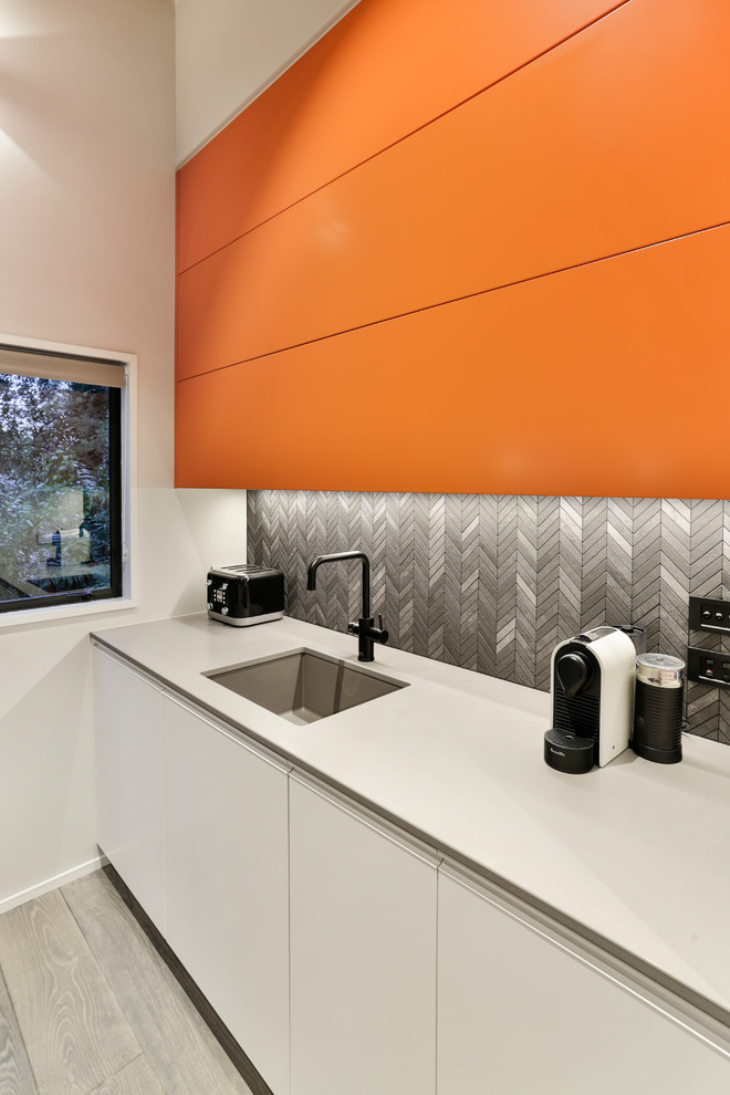 Foto på ett mellanstort funkis grå kök, med en enkel diskho, släta luckor, orange skåp, bänkskiva i kvarts, svart stänkskydd, stänkskydd i porslinskakel, svarta vitvaror, målat trägolv, en köksö och grått golv