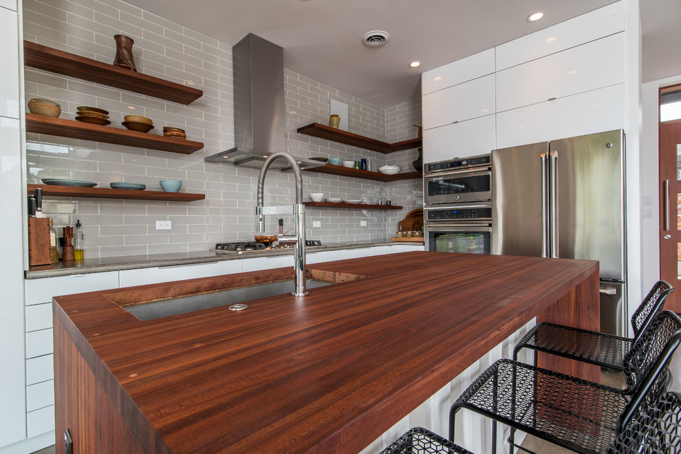 Inspiration for a small modern l-shaped concrete floor and gray floor open concept kitchen remodel in Cleveland with an undermount sink, flat-panel cabinets, white cabinets, wood countertops, gray backsplash, glass tile backsplash, stainless steel appliances and an island