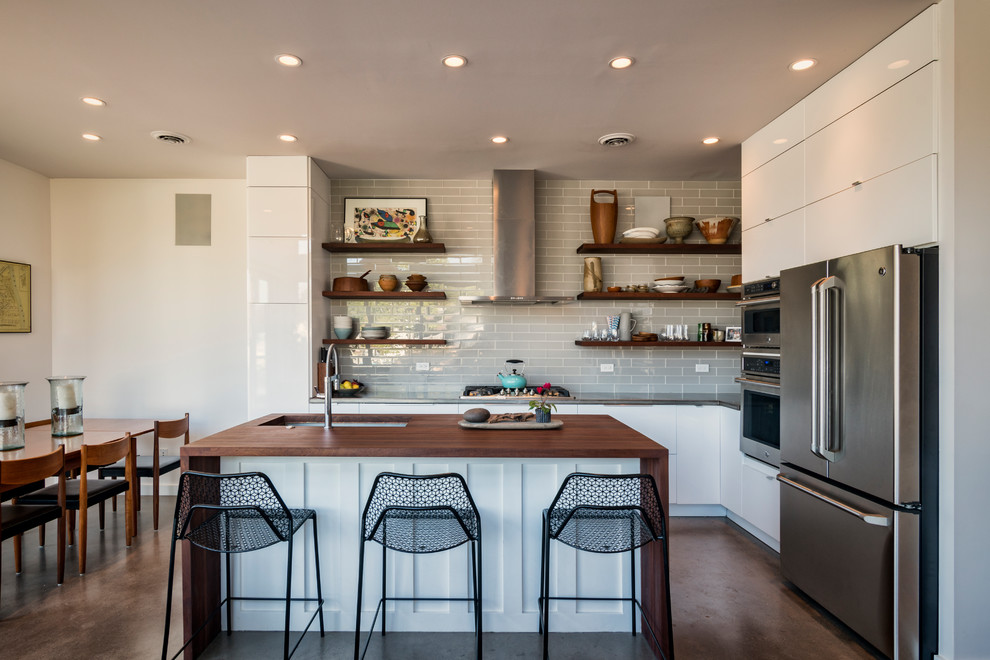 Idéer för ett litet modernt kök, med en undermonterad diskho, släta luckor, vita skåp, träbänkskiva, grått stänkskydd, stänkskydd i glaskakel, rostfria vitvaror, betonggolv, en köksö och grått golv