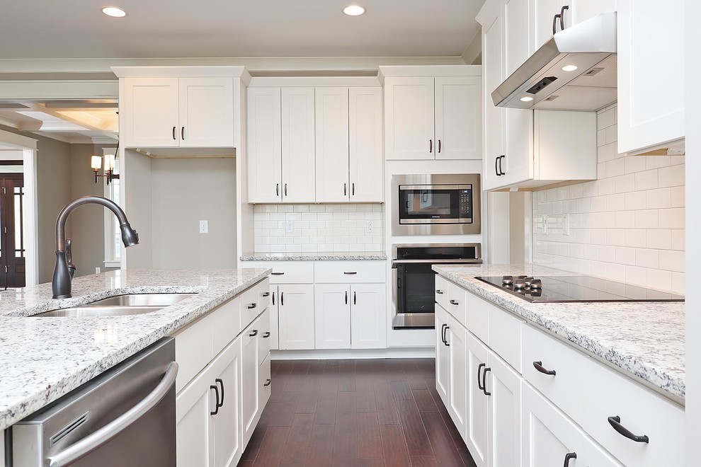 Example of a large classic l-shaped brown floor and vinyl floor eat-in kitchen design in Raleigh with an undermount sink, shaker cabinets, white cabinets, granite countertops, white backsplash, stainless steel appliances, an island, multicolored countertops and subway tile backsplash