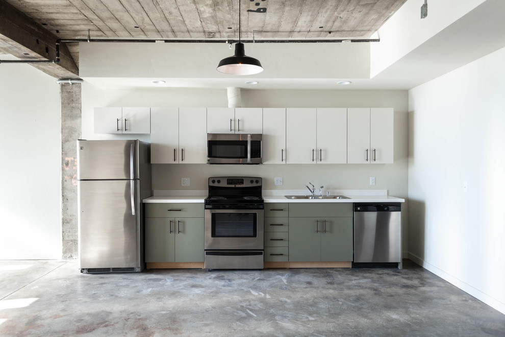 Photo of an industrial single-wall open plan kitchen in Sacramento with a double-bowl sink, flat-panel cabinets, green cabinets, engineered stone countertops, stainless steel appliances and concrete flooring.
