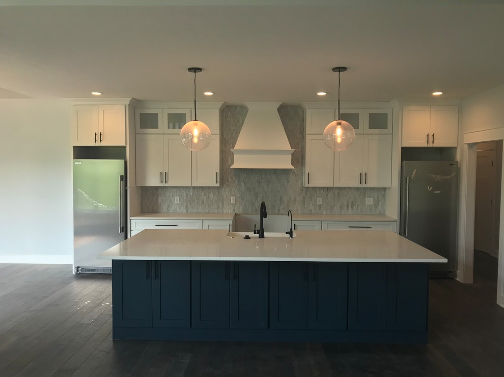 Example of a large transitional single-wall dark wood floor and brown floor open concept kitchen design in Other with a farmhouse sink, shaker cabinets, white cabinets, solid surface countertops, white backsplash, marble backsplash, stainless steel appliances, an island and white countertops