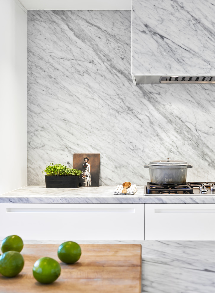 Immagine di una cucina minimalista di medie dimensioni con ante lisce, top in marmo, paraspruzzi bianco, paraspruzzi in marmo, elettrodomestici in acciaio inossidabile, parquet chiaro e top bianco