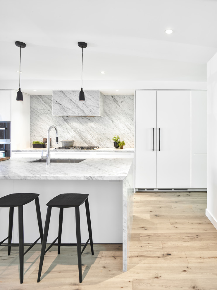 Photo of a medium sized contemporary galley open plan kitchen in Toronto with flat-panel cabinets, marble worktops, white splashback, marble splashback, stainless steel appliances, light hardwood flooring, an island, white worktops, a submerged sink, white cabinets and beige floors.