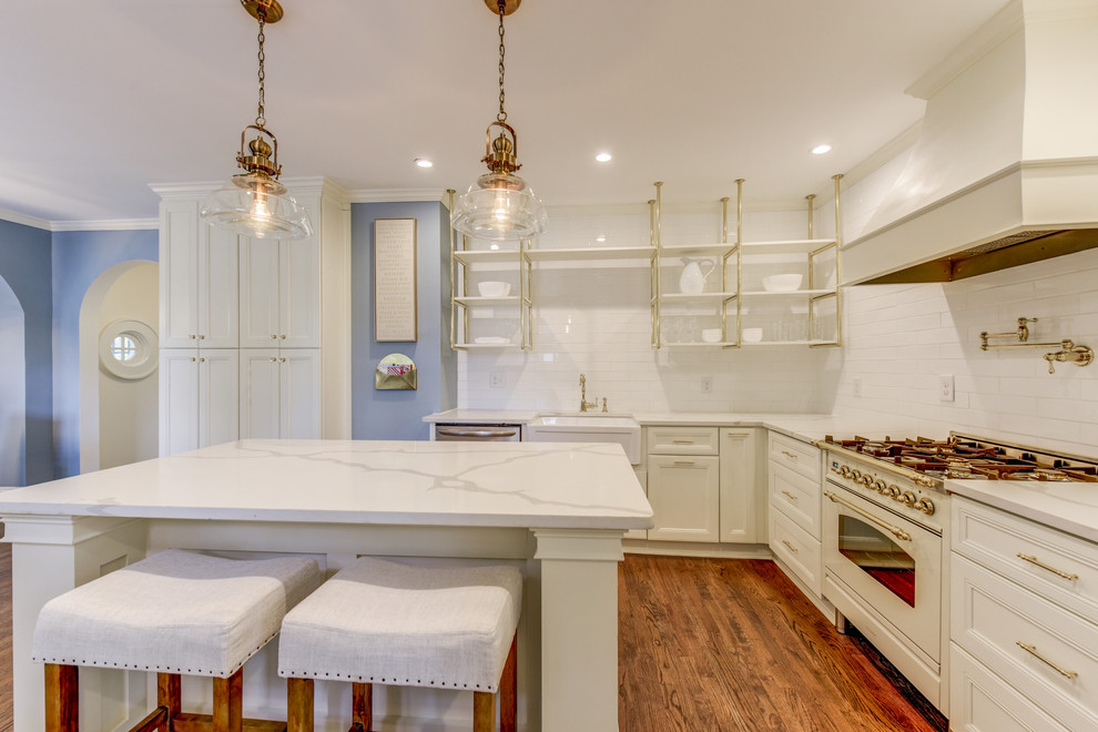 Inspiration for a large transitional l-shaped medium tone wood floor and brown floor kitchen remodel in Atlanta with a farmhouse sink, recessed-panel cabinets, white cabinets, marble countertops, white backsplash, marble backsplash, stainless steel appliances, an island and white countertops