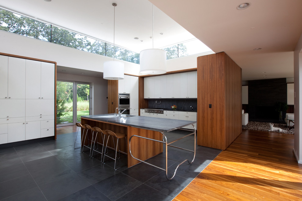 Immagine di una cucina minimalista con ante lisce, ante bianche, paraspruzzi in lastra di pietra, elettrodomestici in acciaio inossidabile e pavimento in ardesia