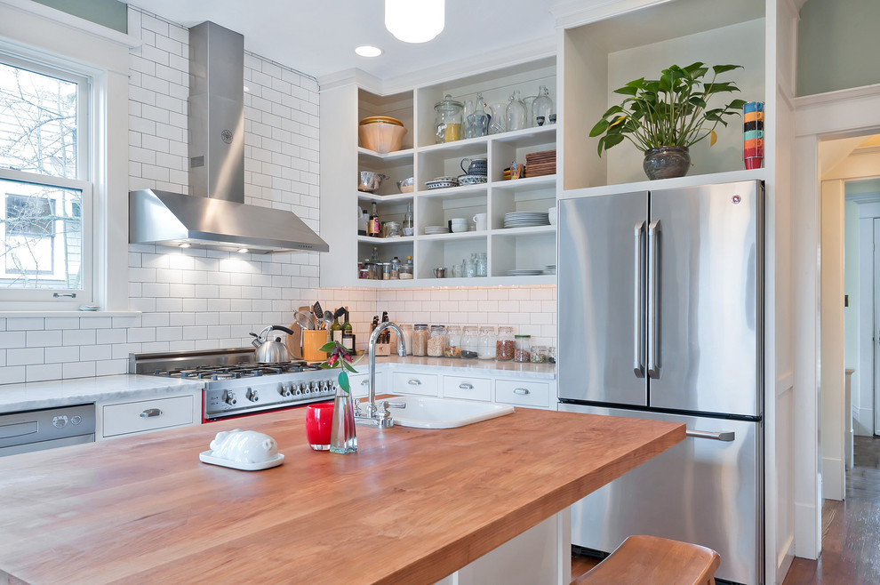 Example of a mid-sized country u-shaped carpeted and brown floor enclosed kitchen design in Seattle with a farmhouse sink, shaker cabinets, white cabinets, wood countertops, white backsplash, subway tile backsplash, stainless steel appliances, an island and brown countertops