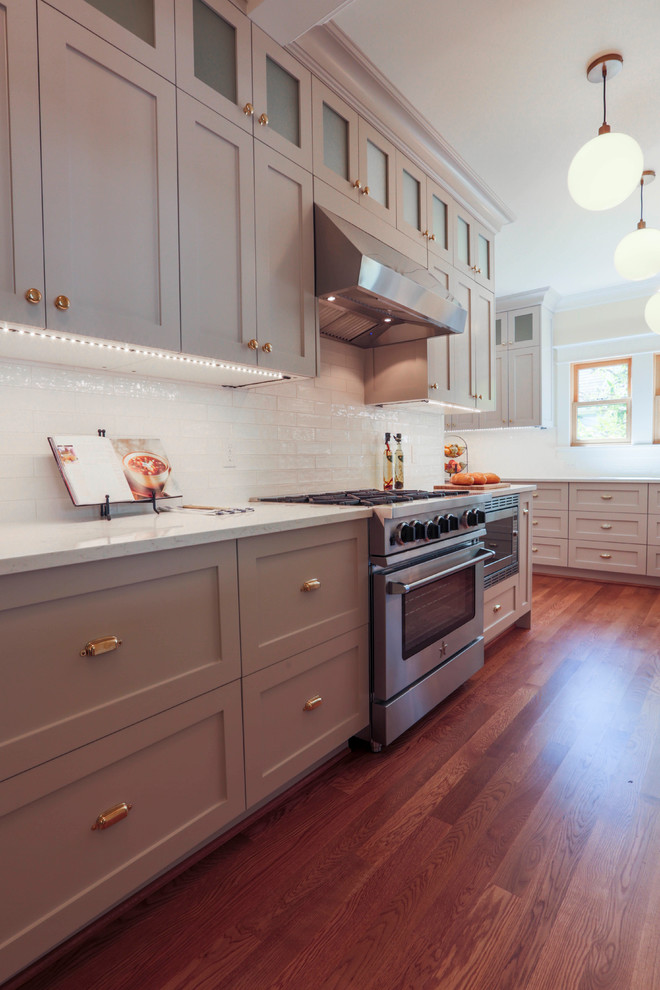 Small traditional l-shaped open plan kitchen in Seattle with a submerged sink, shaker cabinets, grey cabinets, engineered stone countertops, white splashback, metro tiled splashback, stainless steel appliances, medium hardwood flooring and brown floors.