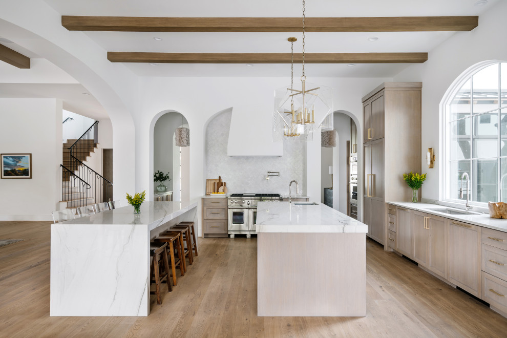 Design ideas for an expansive mediterranean l-shaped kitchen in Austin with a submerged sink, shaker cabinets, beige cabinets, white splashback, integrated appliances, light hardwood flooring, multiple islands, beige floors and white worktops.