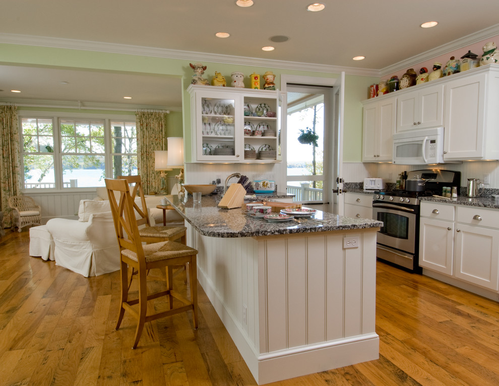 Example of a mid-sized beach style u-shaped medium tone wood floor and brown floor eat-in kitchen design in Other with flat-panel cabinets, white cabinets, granite countertops, stainless steel appliances, an island, a double-bowl sink and multicolored countertops