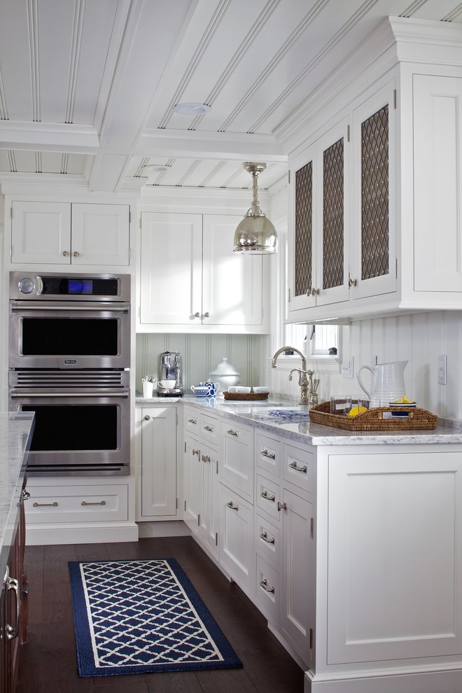 Foto på ett mellanstort funkis grå kök, med en undermonterad diskho, luckor med profilerade fronter, vita skåp, granitbänkskiva, vitt stänkskydd, stänkskydd i trä, rostfria vitvaror, mörkt trägolv, en köksö och brunt golv