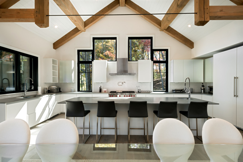 This is an example of a contemporary cream and black u-shaped kitchen/diner in Other with a submerged sink, flat-panel cabinets, white cabinets, white splashback, integrated appliances, an island, brown floors, grey worktops and a vaulted ceiling.
