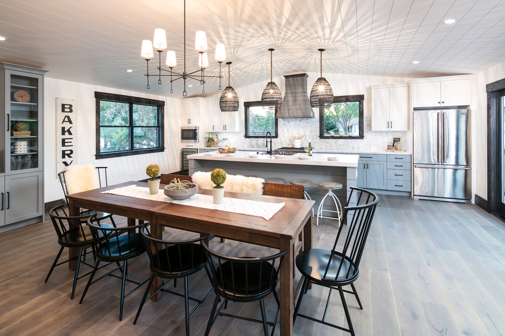 Design ideas for a large rural single-wall kitchen/diner in San Francisco with a belfast sink, shaker cabinets, grey cabinets, composite countertops, multi-coloured splashback, ceramic splashback, stainless steel appliances, medium hardwood flooring, an island, brown floors and white worktops.