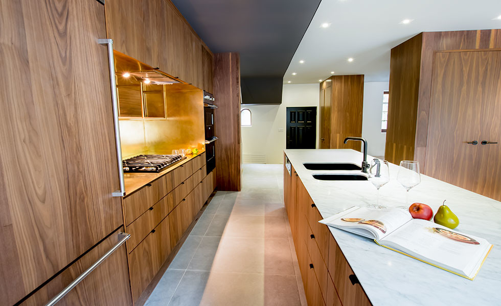 Large modern galley open plan kitchen in Montreal with a submerged sink, flat-panel cabinets, dark wood cabinets, engineered stone countertops, metallic splashback, black appliances, metal splashback, porcelain flooring and an island.