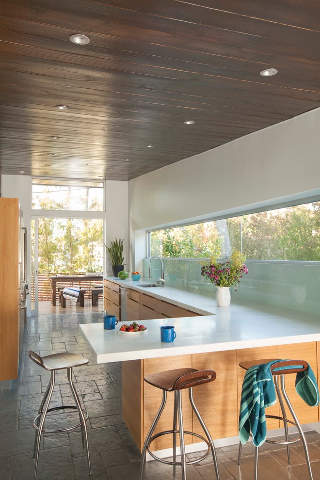 Moderne Küche in L-Form mit Unterbauwaschbecken, flächenbündigen Schrankfronten, hellbraunen Holzschränken, Küchenrückwand in Grün, Glasrückwand und Halbinsel in Los Angeles