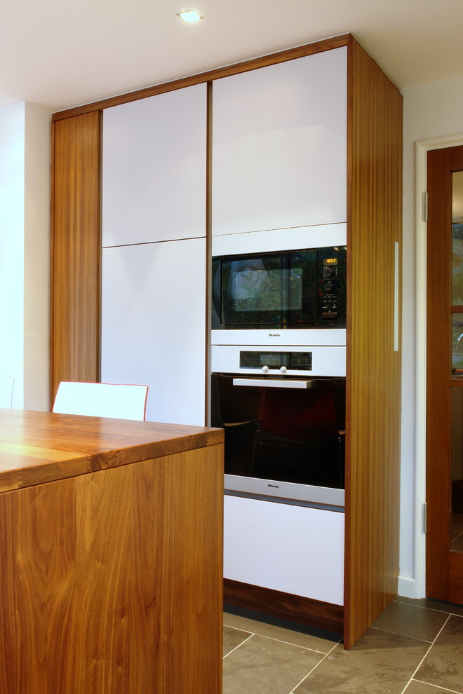 Photo of a medium sized contemporary u-shaped kitchen in London with a submerged sink, flat-panel cabinets, white cabinets, wood worktops, white splashback, glass sheet splashback, stainless steel appliances, ceramic flooring and an island.