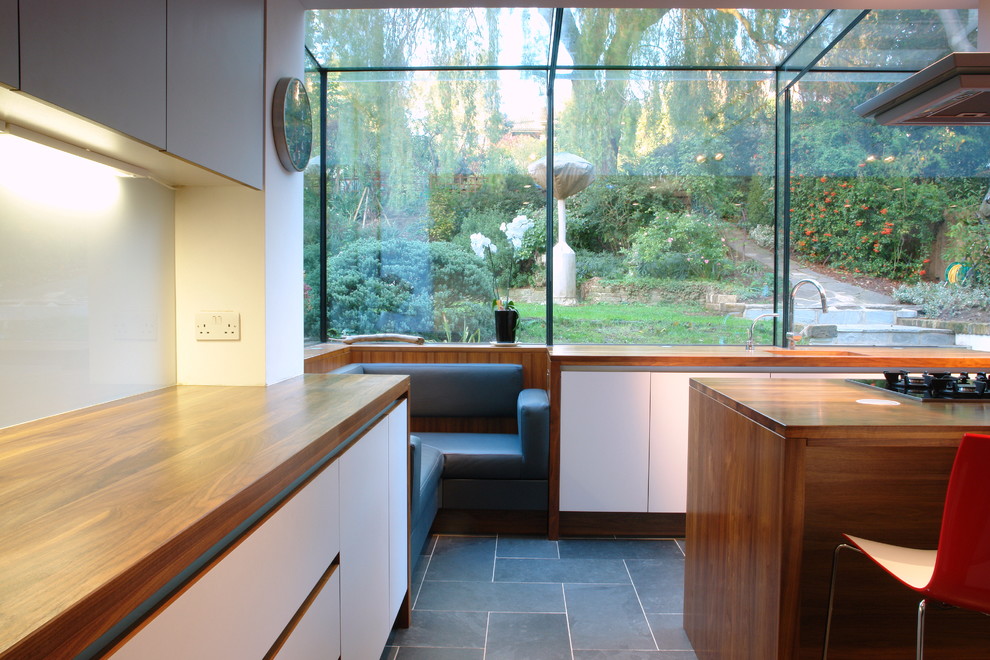 Inspiration for a medium sized contemporary u-shaped kitchen in London with a submerged sink, flat-panel cabinets, white cabinets, wood worktops, white splashback, glass sheet splashback, stainless steel appliances, ceramic flooring and an island.