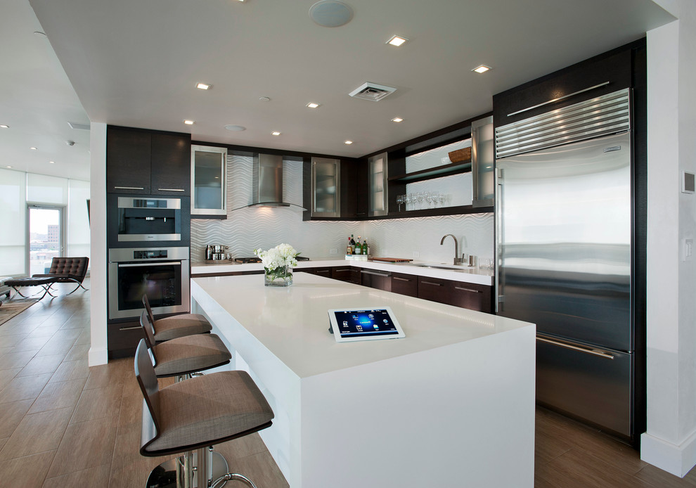 Inspiration for a large modern l-shaped porcelain tile and brown floor kitchen remodel in Philadelphia with an undermount sink, flat-panel cabinets, black cabinets, solid surface countertops, white backsplash, stainless steel appliances and an island