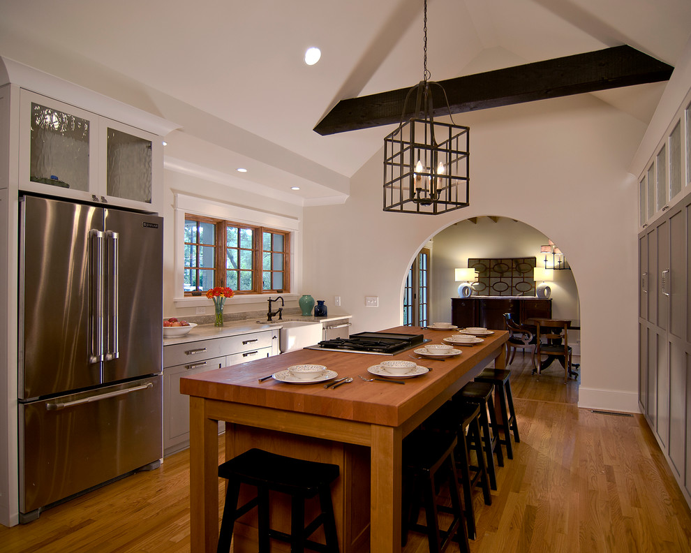 Large trendy u-shaped light wood floor and brown floor enclosed kitchen photo in Charlotte with recessed-panel cabinets, an island, a farmhouse sink, white cabinets, wood countertops and stainless steel appliances